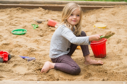 Mädchen spielt im Sandkasten mit Eimer und Schaufel