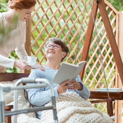 Ältere Frau mit Gehhilfe sitzt im Garten und liest