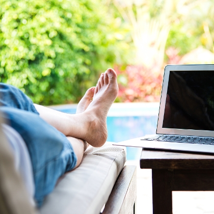 Person liegt mit Laptop auf einer Gartenliege vorm Pool