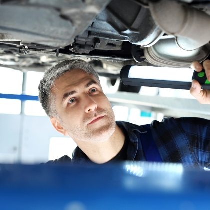 Mechaniker leuchtet mit einer Werkstattlampe auf eine Autounterbodenplatte